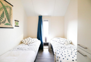 Helles Zimmer mit zwei Einzelbetten, Pflanzenbildern und Vorhang, Beach House 4, Marina Strandbad, Niederlande.
