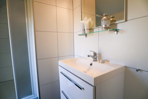 Baño moderno con lavabo blanco, espejo, estante de vidrio y ducha en Beach House 4 en Marina Strandbad, Países Bajos.