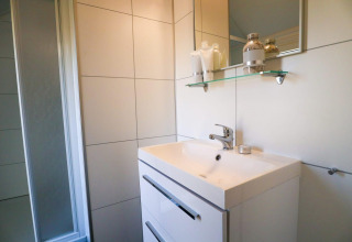 Salle de bain moderne avec lavabo blanc, miroir, étagère en verre et douche au Beach House 4, Marina Strandbad, Pays-Bas.