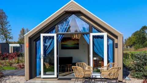 Beach House 4 lodge en Marina Strandbad, Países Bajos, con puertas abiertas, cortinas azules y muebles de jardín.