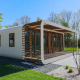 Moderne lodge med buede kanter og træpaneler, omgivet af grønt græs og træer på en solrig dag.