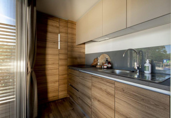 Modern lodge kitchen featuring wood cabinets, sleek black countertop, and large window letting in sunlight.