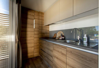 Zeitgemäße Küchenzeile in einer Lodge mit Holzfronten, Hängeschränken und großem Fenster im Sonnenlicht.