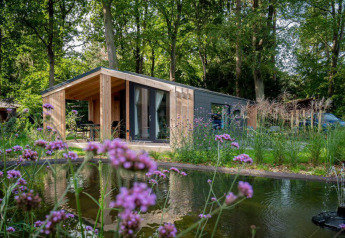 Panorama Cottage 4-lodge ved Marina Strandbad i Holland, omgivet af træer, blomster og en dam.