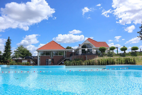 Alojamiento glamping con casa moderna y gran piscina bajo un cielo azul con nubes esponjosas.