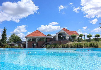 Alojamiento glamping con casa moderna y gran piscina bajo un cielo azul con nubes esponjosas.