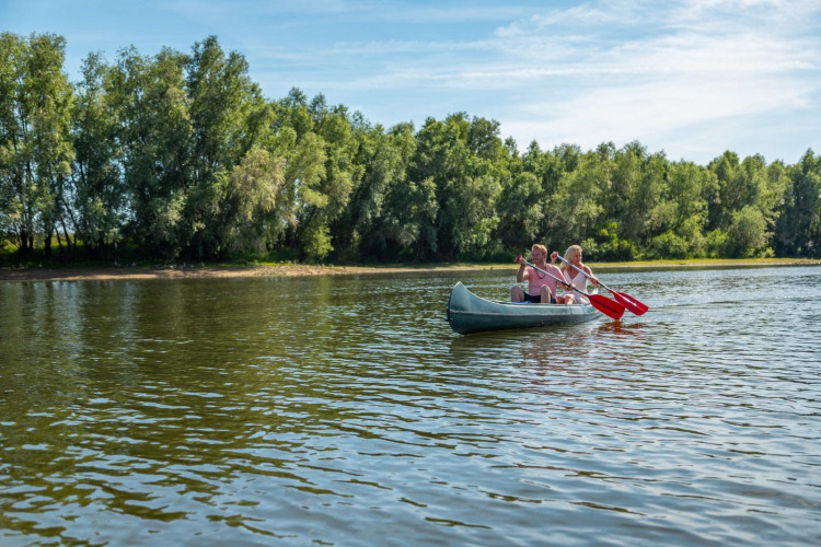 Zwei Personen paddeln in einem Kanu auf einem ruhigen See, umgeben von Bäumen beim Glampingurlaub.