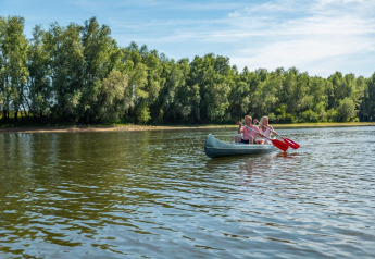 Dos personas reman en una canoa sobre un lago tranquilo rodeado de árboles durante una estancia de glamping.