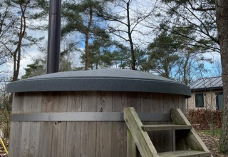 Udendørs træfyret vildmarksbad med en trappe og sort skorsten ved en lodge omgivet af træer og hytter.