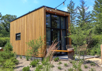 Moderne tiny house kaldet Tiny House 2 med træfacade og store vinduer midt i grønt, naturskønt område.