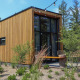 Moderne tiny house kaldet Tiny House 2 med træfacade og store vinduer midt i grønt, naturskønt område.