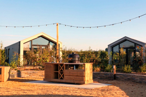 Cucina all'aperto davanti a Tiny House 2 al Marina Strandbad nei Paesi Bassi, luci sospese e piante verdi.