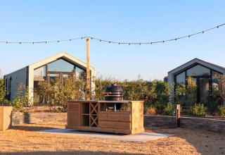 Cucina all'aperto davanti a Tiny House 2 al Marina Strandbad nei Paesi Bassi, luci sospese e piante verdi.