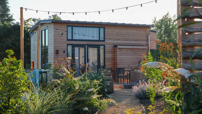 Tiny House 4 lodge with string lights, surrounded by lush gardens and patio seating in a tranquil setting.