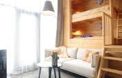 Licht interieur met houten stapelbedden, comfortabele bank, tafel en grote ramen in Tiny House 4, Nederland.