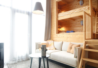 Lyst interiør af en lodge med køjesenge i træ, sofa, bord og store vinduer i Tiny House 4, Holland.