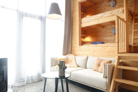 Lyst interiør af en lodge med køjesenge i træ, sofa, bord og store vinduer i Tiny House 4, Holland.