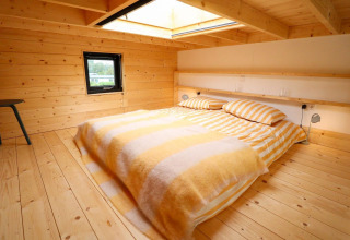 Sfeervolle slaapkamer in Tiny House 4 bij Marina Strandbad, Nederland, met houten bekleding en dakraam.