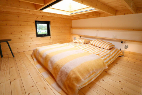 Chambre confortable dans Tiny House 4 à Marina Strandbad, Pays-Bas, avec lambris bois et puits de lumière.