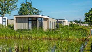 Lodge Cube la Mer 4 dal design moderno situato sul lago, circondato da vegetazione e cielo azzurro.