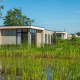 Cube la Mer 4 lodge med moderne design ved søbredden, omgivet af grøn vegetation og blå himmel.