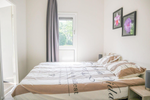 Lichte slaapkamer in Cube la Mer 4, Marina Strandbad, Nederland, met raam, groot bed en bloemenschilderijen aan de muur.