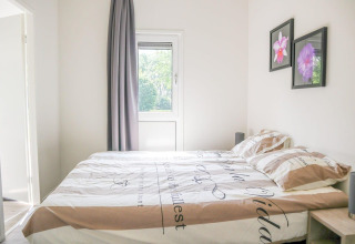 Lichte slaapkamer in Cube la Mer 4, Marina Strandbad, Nederland, met raam, groot bed en bloemenschilderijen aan de muur.