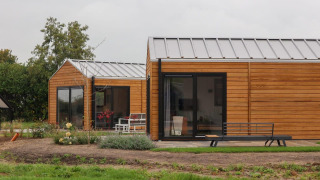 Wellness Lodge 2 moderna con revestimiento de madera, grandes ventanales y jardín verde natural.