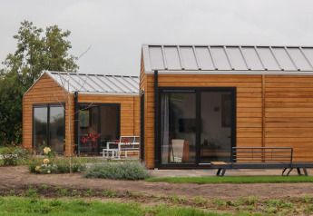 Moderne Wellness Lodge 2 met houten buitenkant, grote glazen deuren en een groene tuin in de natuur.