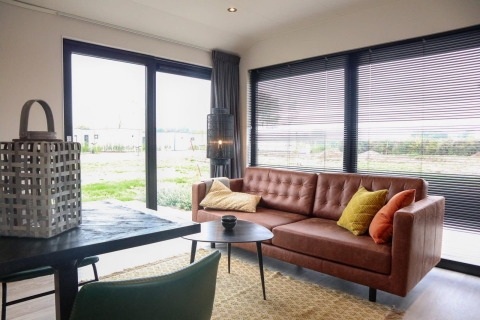 Soggiorno moderno nella Wellness Lodge 2 al Marina Strandbad, Paesi Bassi, con divano e ampie finestre.