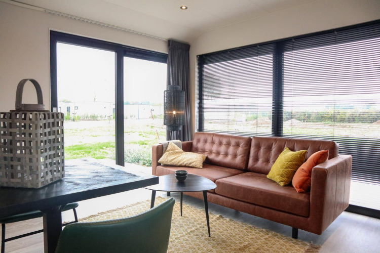 Salón moderno en Wellness Lodge 2 en Marina Strandbad, Países Bajos, con sofá y grandes ventanales.