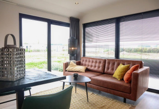 Soggiorno moderno nella Wellness Lodge 2 al Marina Strandbad, Paesi Bassi, con divano e ampie finestre.