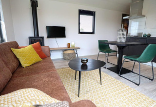 Sala moderna con sofá marrón, cojines de colores, mesa, sillas verdes y estufa en Wellness Lodge 2.