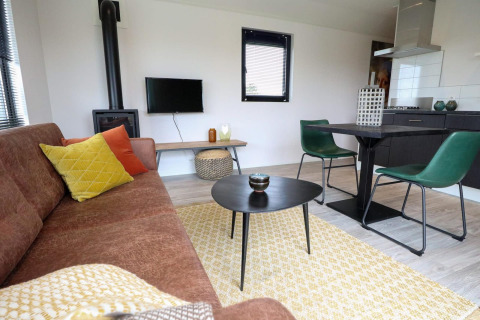 Sala moderna con sofá marrón, cojines de colores, mesa, sillas verdes y estufa en Wellness Lodge 2.