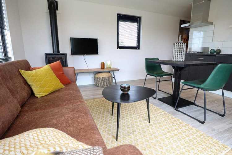 Sala moderna con sofá marrón, cojines de colores, mesa, sillas verdes y estufa en Wellness Lodge 2.