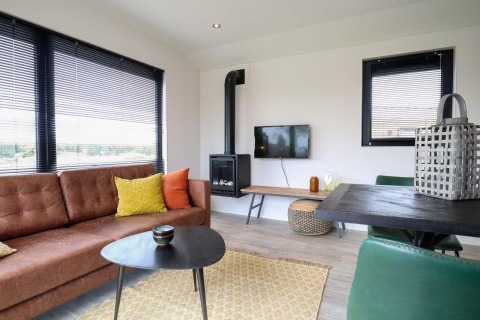 Modernes Wohnzimmer im Wellness Lodge 2, Marina Strandbad Niederlande, mit Sofa, TV, Ofen und großen Fenstern.