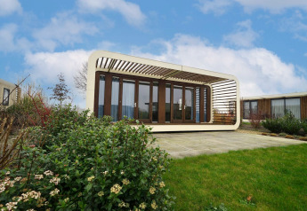 Lodge Modus 4 moderno con pareti in vetro e struttura bianca, situato in un giardino curato sotto un cielo azzurro.