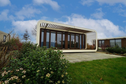 Stijlvolle Modus 4 lodge met glazen voorzijde en unieke structuur, omringd door verzorgd groen onder blauwe lucht.