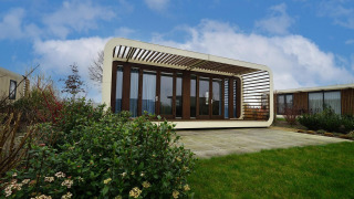 Contemporary Modus 4 lodge with glass walls and white frame, standing in a landscaped garden under blue sky.