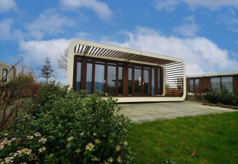 Contemporary Modus 4 lodge with glass walls and white frame, standing in a landscaped garden under blue sky.