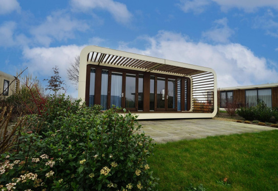 Stijlvolle Modus 4 lodge met glazen voorzijde en unieke structuur, omringd door verzorgd groen onder blauwe lucht.
