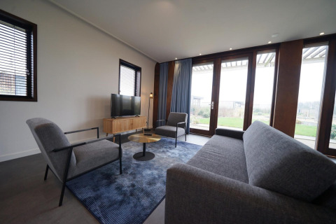 Moderne leefruimte in Modus 4-lodge bij Marina Strandbad, Nederland, met grote ramen en grijze zetels.