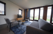 Modern living room in the Modus 4 lodge at Marina Strandbad, Netherlands, with large windows and grey furniture.