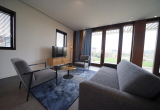 Moderne leefruimte in Modus 4-lodge bij Marina Strandbad, Nederland, met grote ramen en grijze zetels.