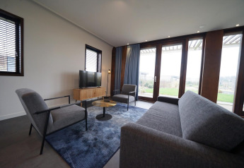 Modern living room in the Modus 4 lodge at Marina Strandbad, Netherlands, with large windows and grey furniture.