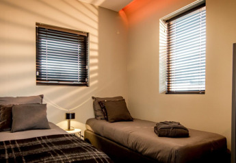 To enkeltsenge og moderne indretning på Modus 4 lodge ved Marina Strandbad i Holland, sollys filtrerer gennem gardiner.