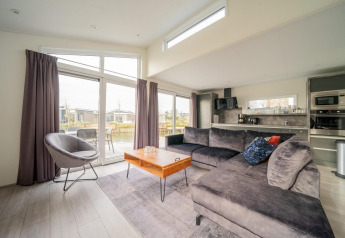 Sala moderna en la cabaña Hackfort 6 en De Kraaijenbergse Plassen, Países Bajos, con sofá y grandes ventanales.