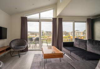 Salon lumineux du lodge Hackfort 6 aux Kraaijenbergse Plassen, Pays-Bas, avec mobilier moderne et grandes fenêtres.