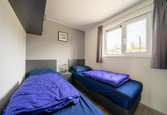 Two single beds with blue bedding in a room at Hackfort 6 lodge, De Kraaijenbergse Plassen, Netherlands.