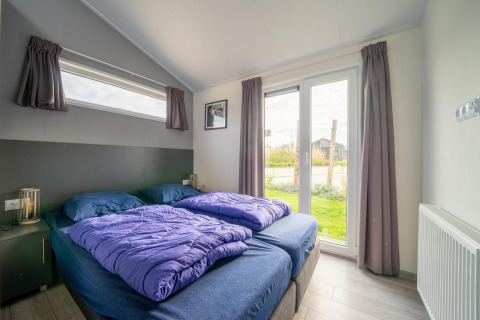 Chambre de lodge moderne avec lit double, couettes violettes et vue sur jardin, Hackfort 6, De Kraaijenbergse Plassen, Pays-Bas.